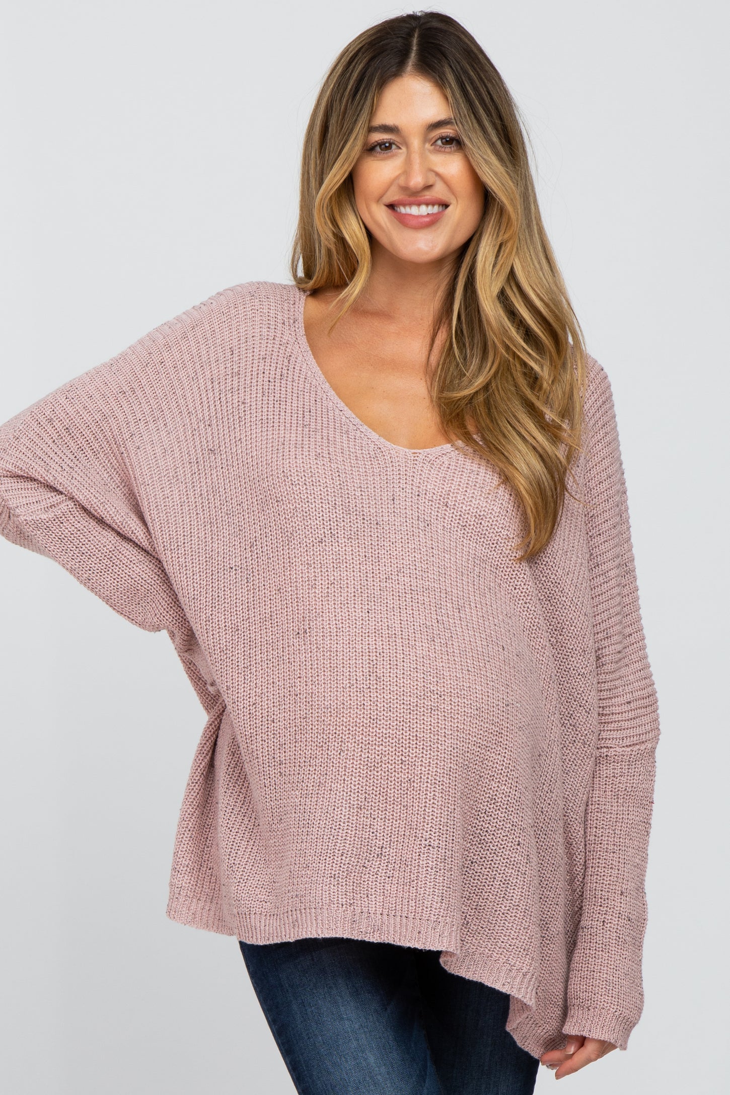woman wearing a light pink oversized maternity sweater with a scoop neck and long sleeves, showing her baby bump