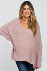 woman wearing a light pink oversized maternity sweater with a scoop neck and long sleeves, showing her baby bump