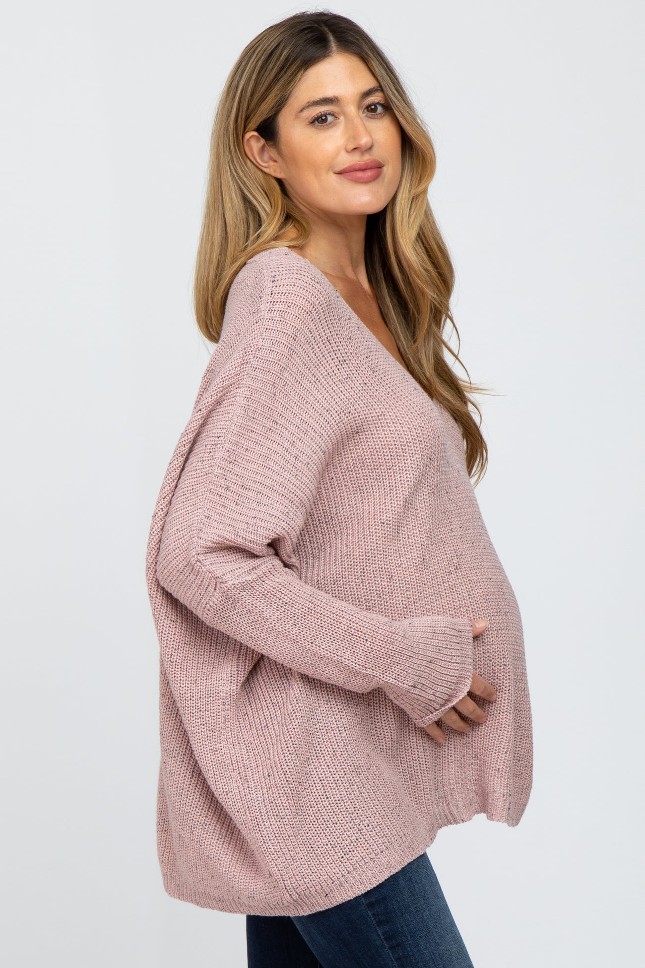 woman wearing a blush pink oversized maternity sweater and cradling her baby bump