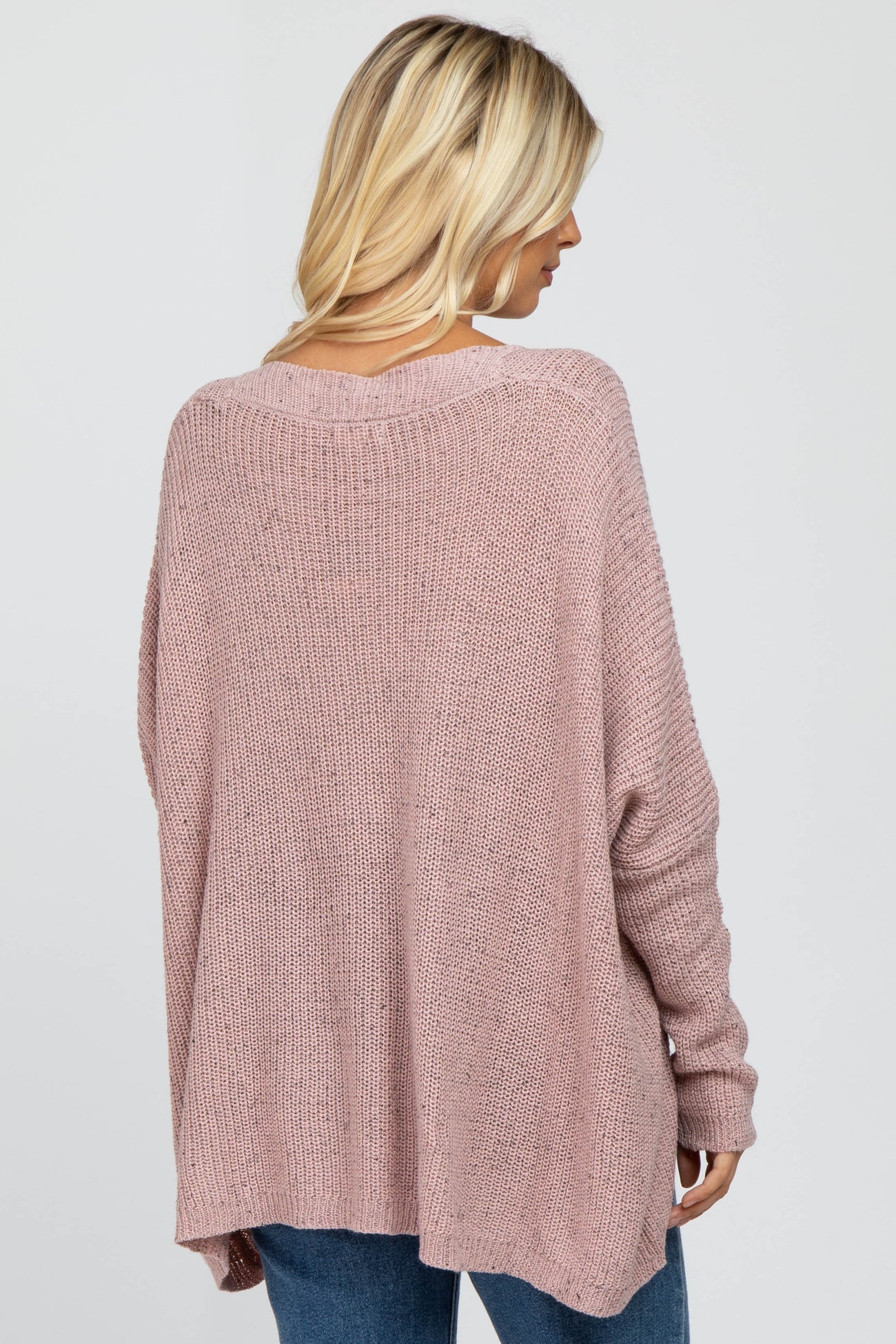 woman wearing a light pink oversized knit sweater from the back, paired with blue jeans
