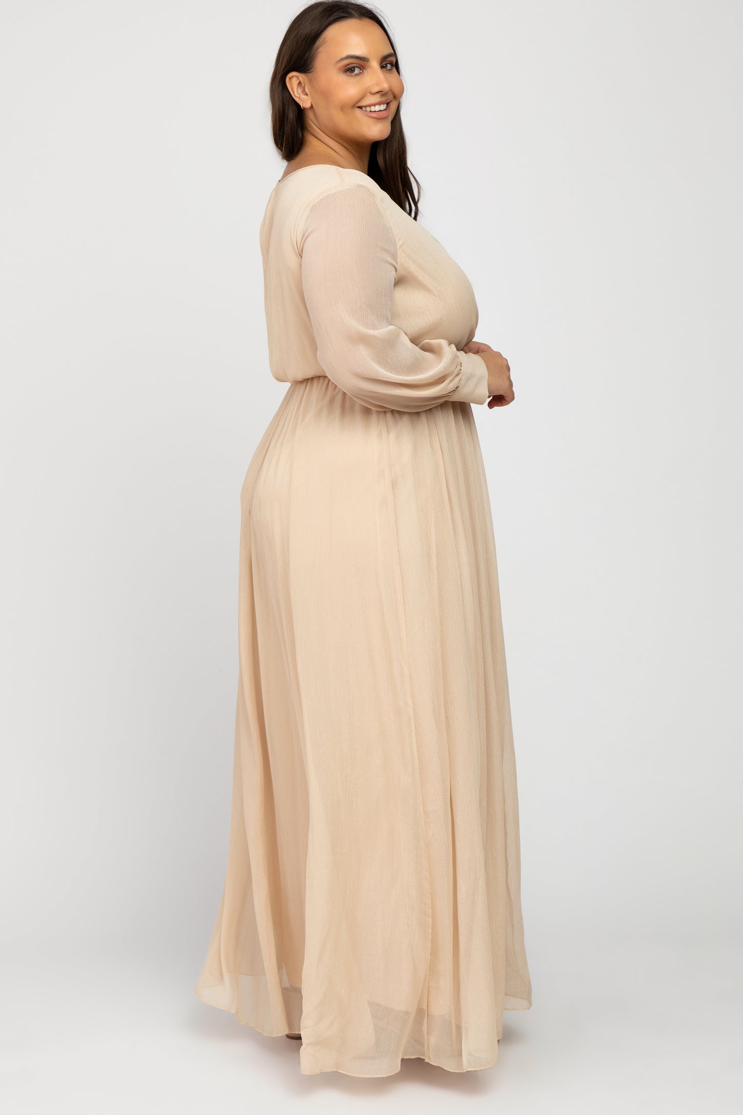 woman wearing a long beige plus-size dress with long sleeves and a flowy skirt, standing in profile