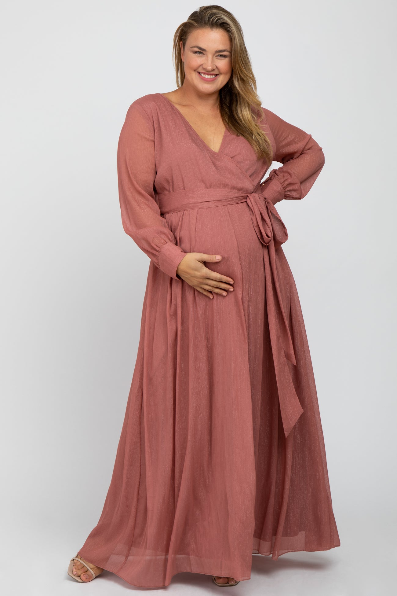 woman wearing a mauve long sleeve maternity plus dress with a tie waist and holding her baby bump