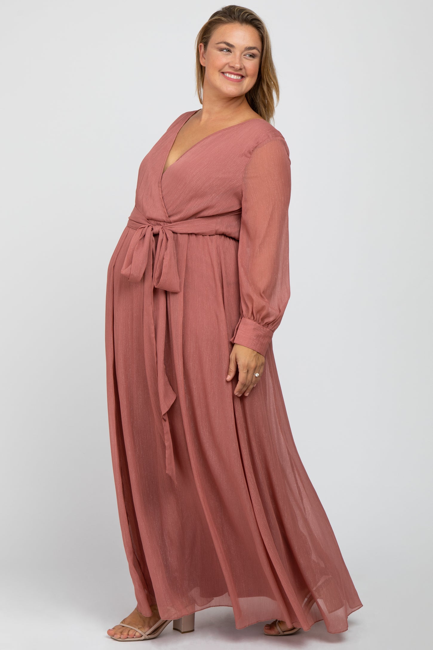 woman wearing a dusty rose floor-length maternity dress with long sleeves and a tie waist, showcasing her baby bump