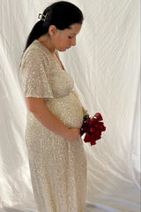 woman wearing a sparkling gold maternity gown and holding a bouquet of red roses, showcasing her baby bump