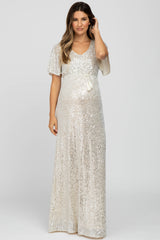 woman wearing a sparkling silver maternity gown with short flutter sleeves and a tie at the waist, showcasing her baby bump
