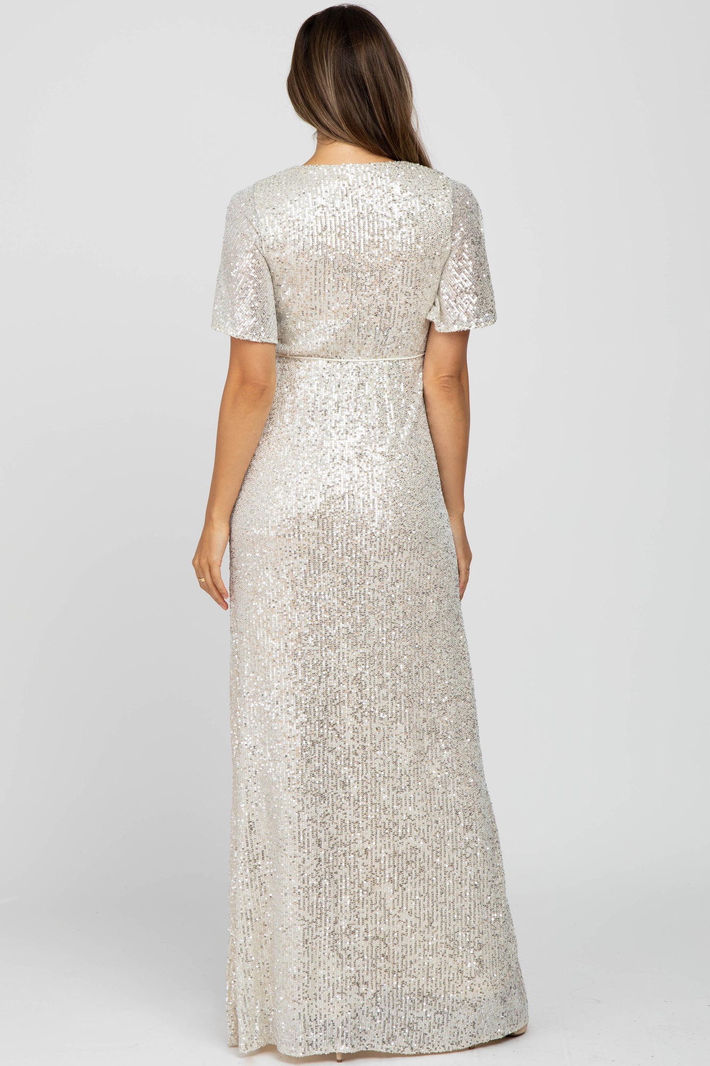 woman wearing a silver sequin maternity gown with short sleeves and a flowing silhouette, showing her baby bump