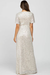 woman wearing a silver sequin maternity gown with short sleeves and a flowing silhouette, showing her baby bump
