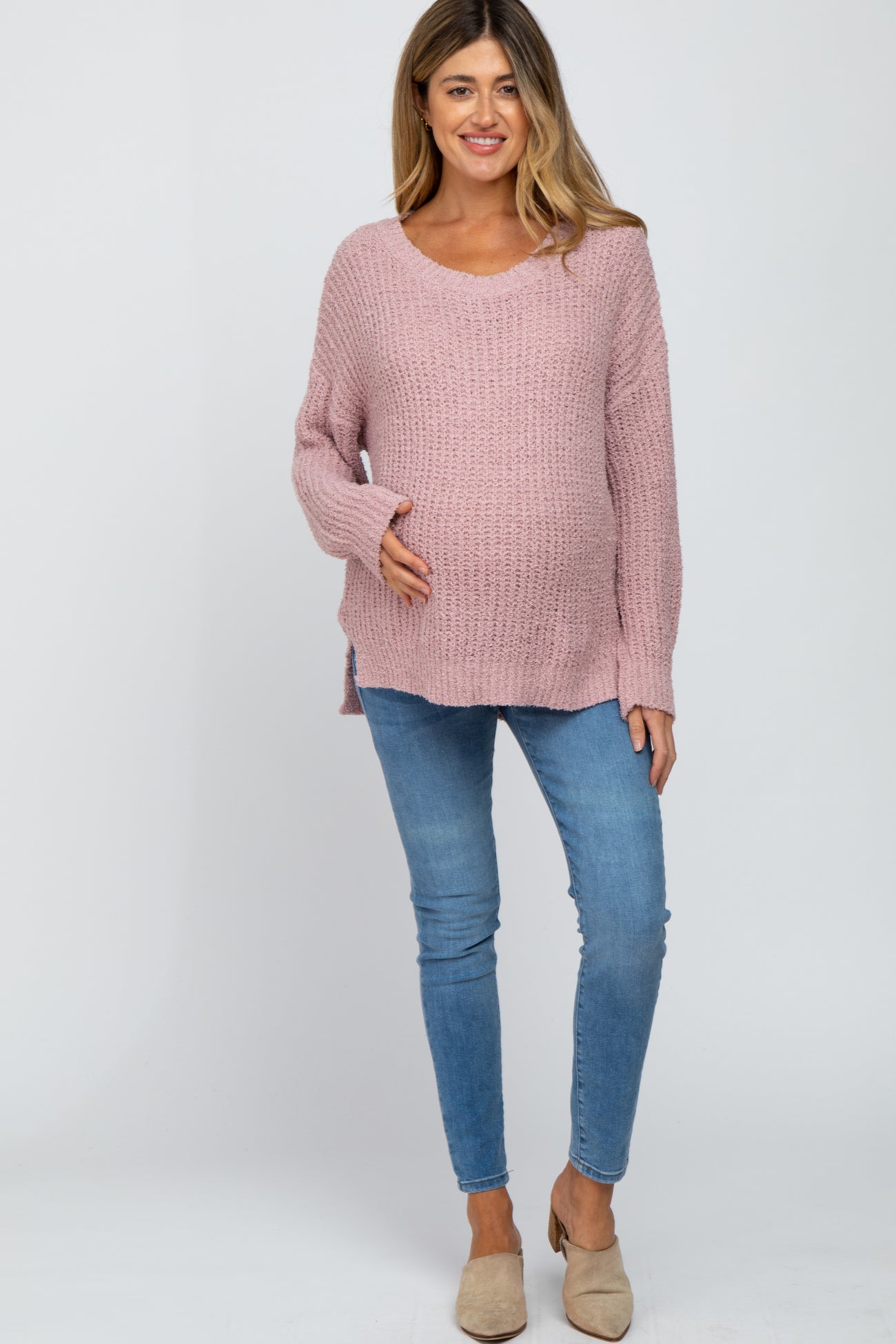 Pregnant woman wearing a pink popcorn knit maternity sweater and blue skinny jeans
