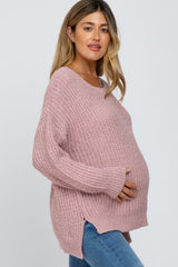 pregnant woman wearing a pink oversized knit maternity sweater and blue jeans