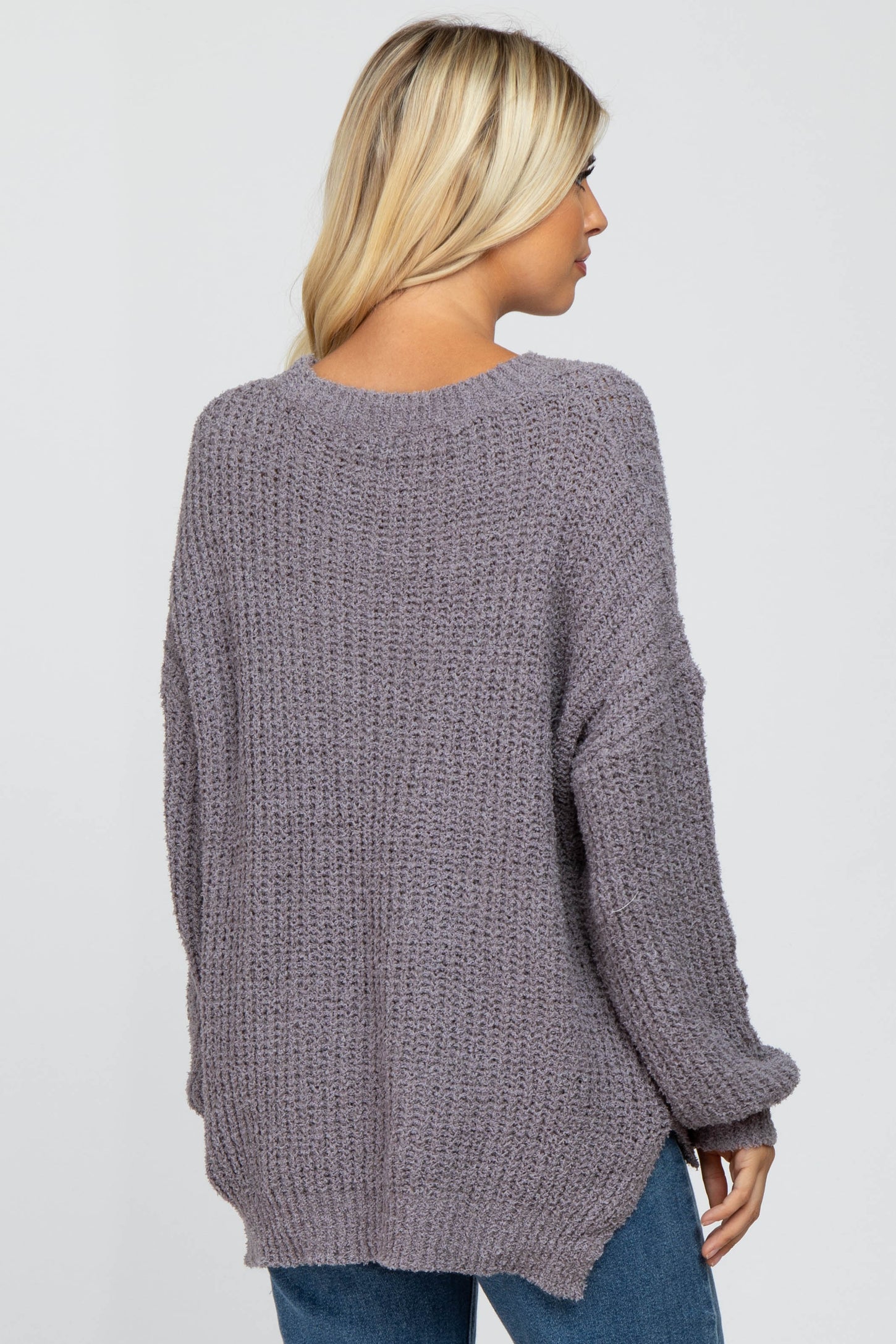 back view of a woman wearing a mauve oversized popcorn knit sweater and blue jeans