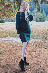 woman wearing a dark green knitted maternity dress with puff sleeves and a visible baby bump in an outdoor setting