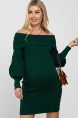woman wearing a dark green off-the-shoulder maternity dress with puff sleeves and holding a small handbag, visible baby bump