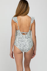 woman wearing a black and white polka dot maternity swimsuit with ruffled straps and a tied back detail