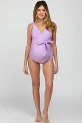 woman wearing a light lavender maternity swimsuit with a wrap design and a bow detail, showing her baby bump