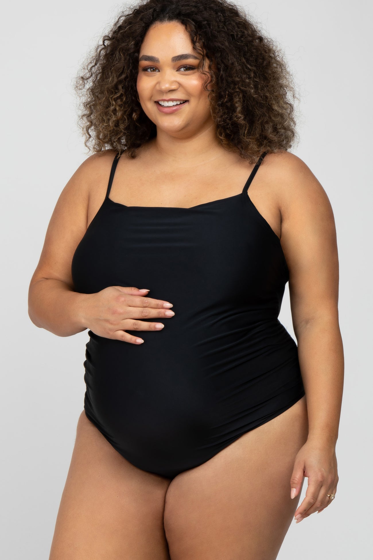 smiling pregnant woman with curly hair wearing a black maternity one-piece swimsuit