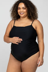 smiling pregnant woman with curly hair wearing a black maternity one-piece swimsuit