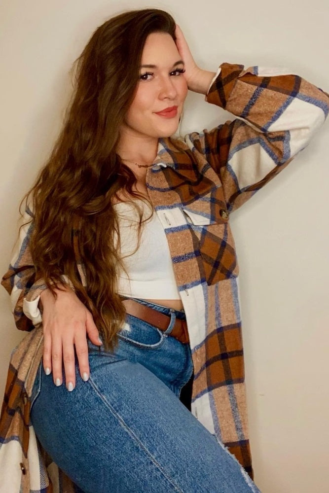 woman with long brown hair wearing a brown and blue plaid shacket over a white crop top and blue jeans