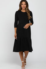 woman wearing a black ribbed long sleeve tiered maternity midi dress with white heels