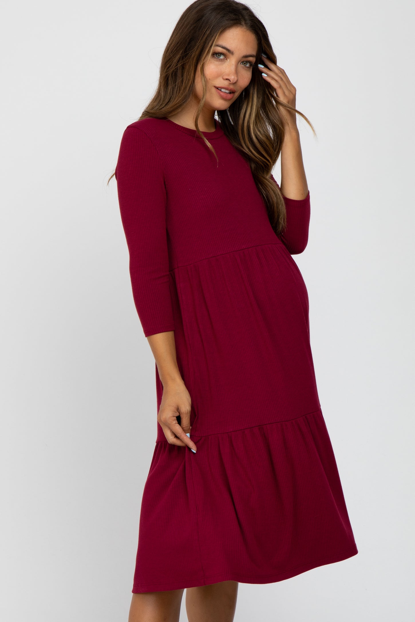 woman wearing a burgundy maternity dress with three-quarter sleeves and a tiered skirt, showing her baby bump