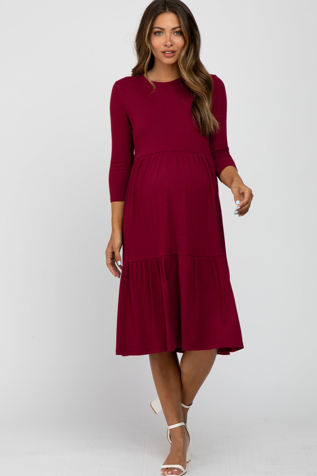 woman wearing a burgundy ribbed long sleeve tiered maternity midi dress with white heels