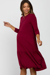 woman wearing a burgundy ribbed maternity dress with a tiered skirt and three-quarter sleeves, showing her baby bump