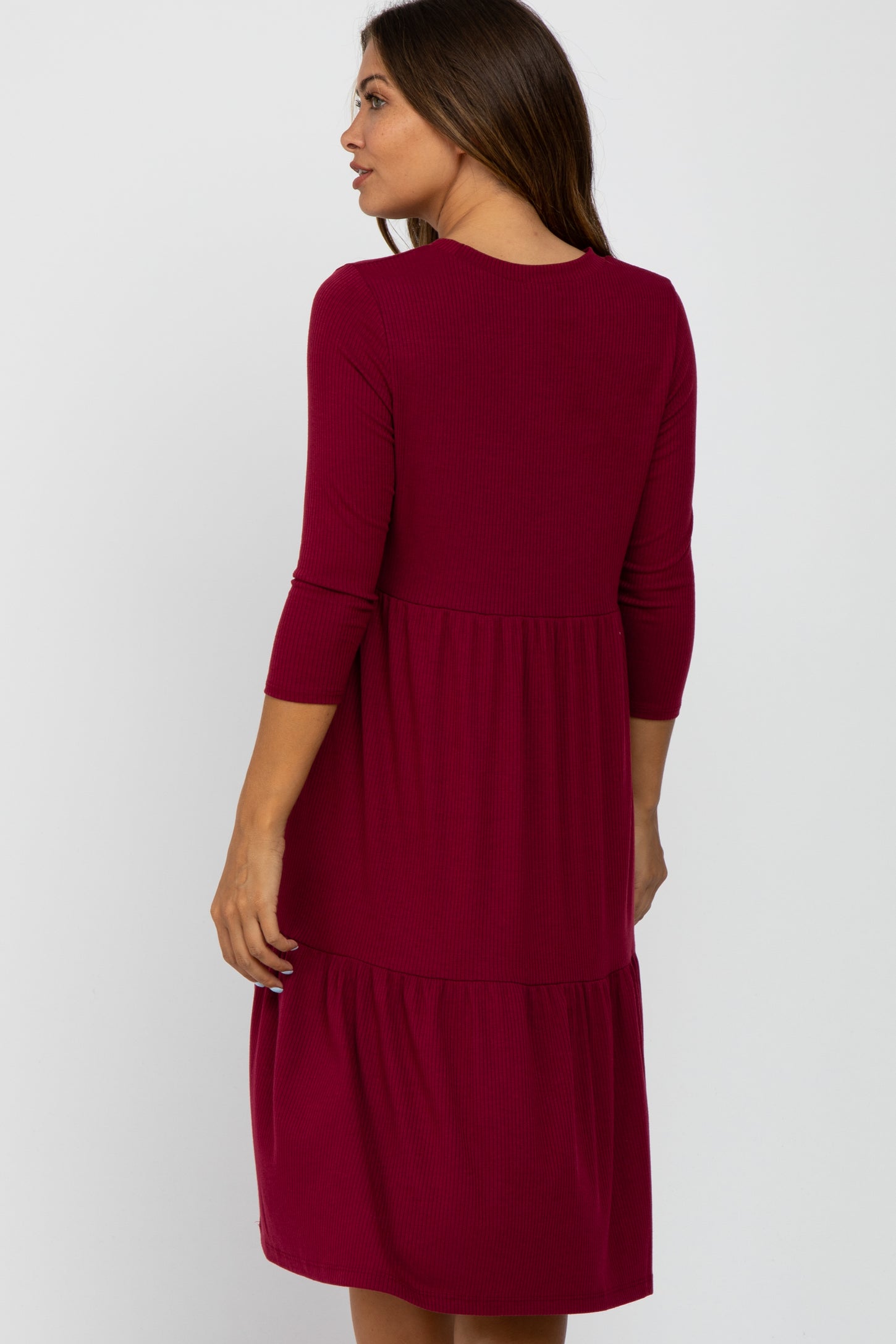 woman wearing a burgundy three-quarter sleeve maternity dress with a tiered skirt and ribbed fabric from the back