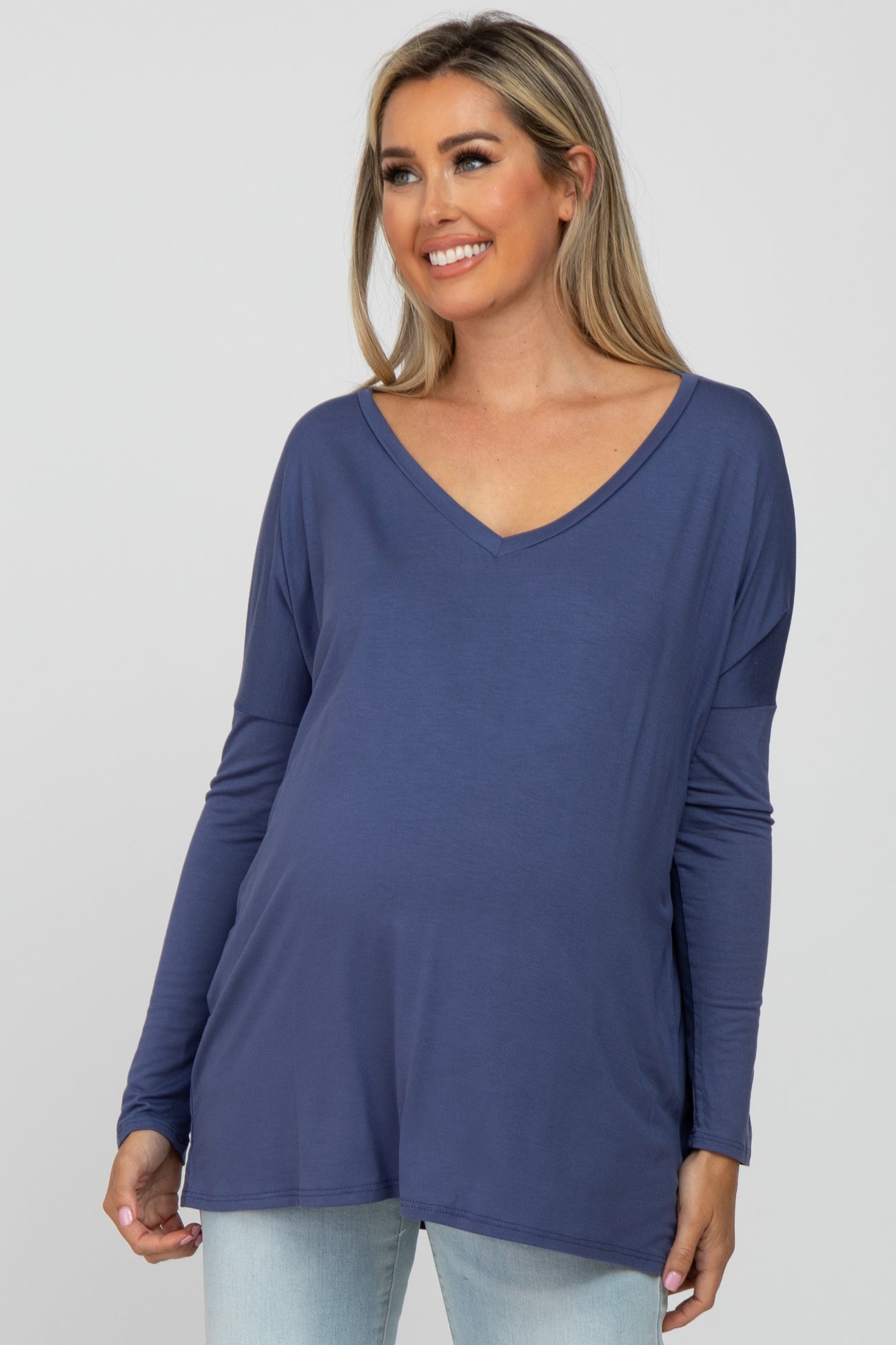 Smiling pregnant woman wearing a blue long sleeve v-neck maternity top and light wash jeans