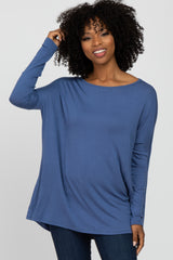 Woman with curly hair wearing a long-sleeved blue tunic top and dark jeans against a white background