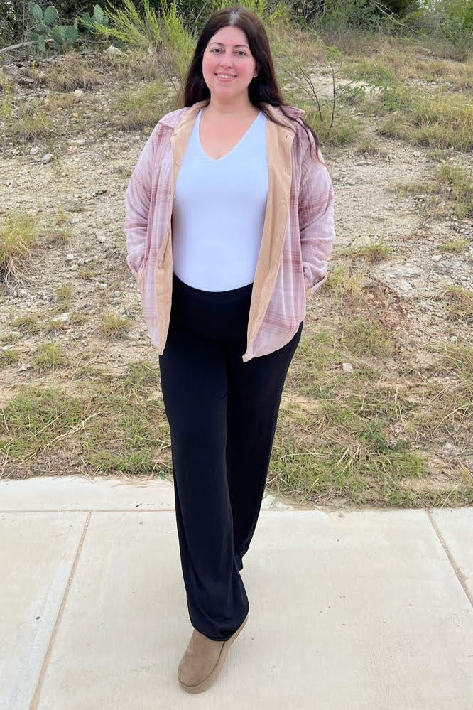 woman wearing pink plaid flannel shirt over white top and black wide leg pants standing outdoors