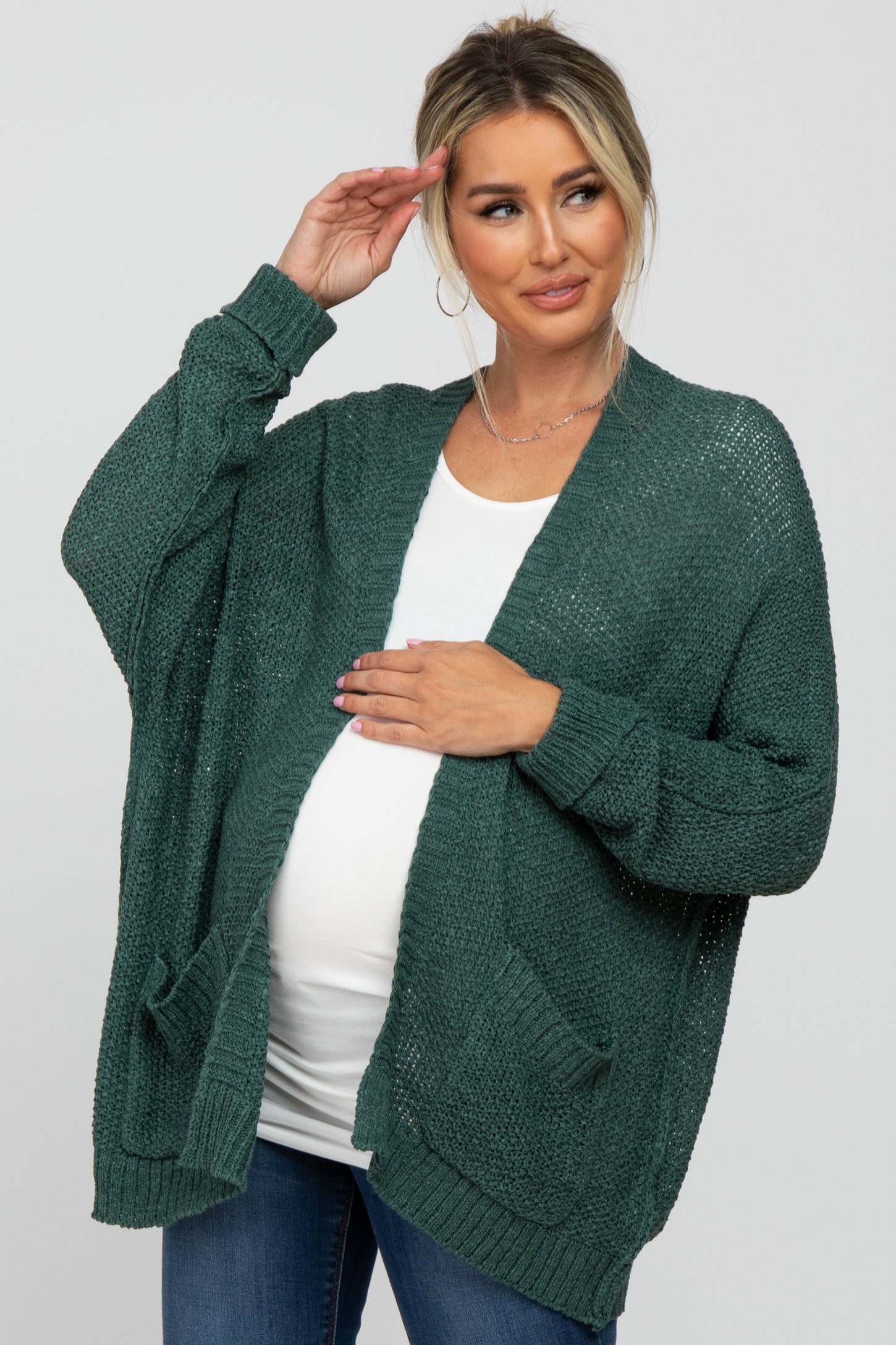 Pregnant woman wearing a dark green oversized knit maternity cardigan over a white top and jeans