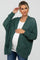 Pregnant woman wearing a dark green oversized knit maternity cardigan over a white top and jeans