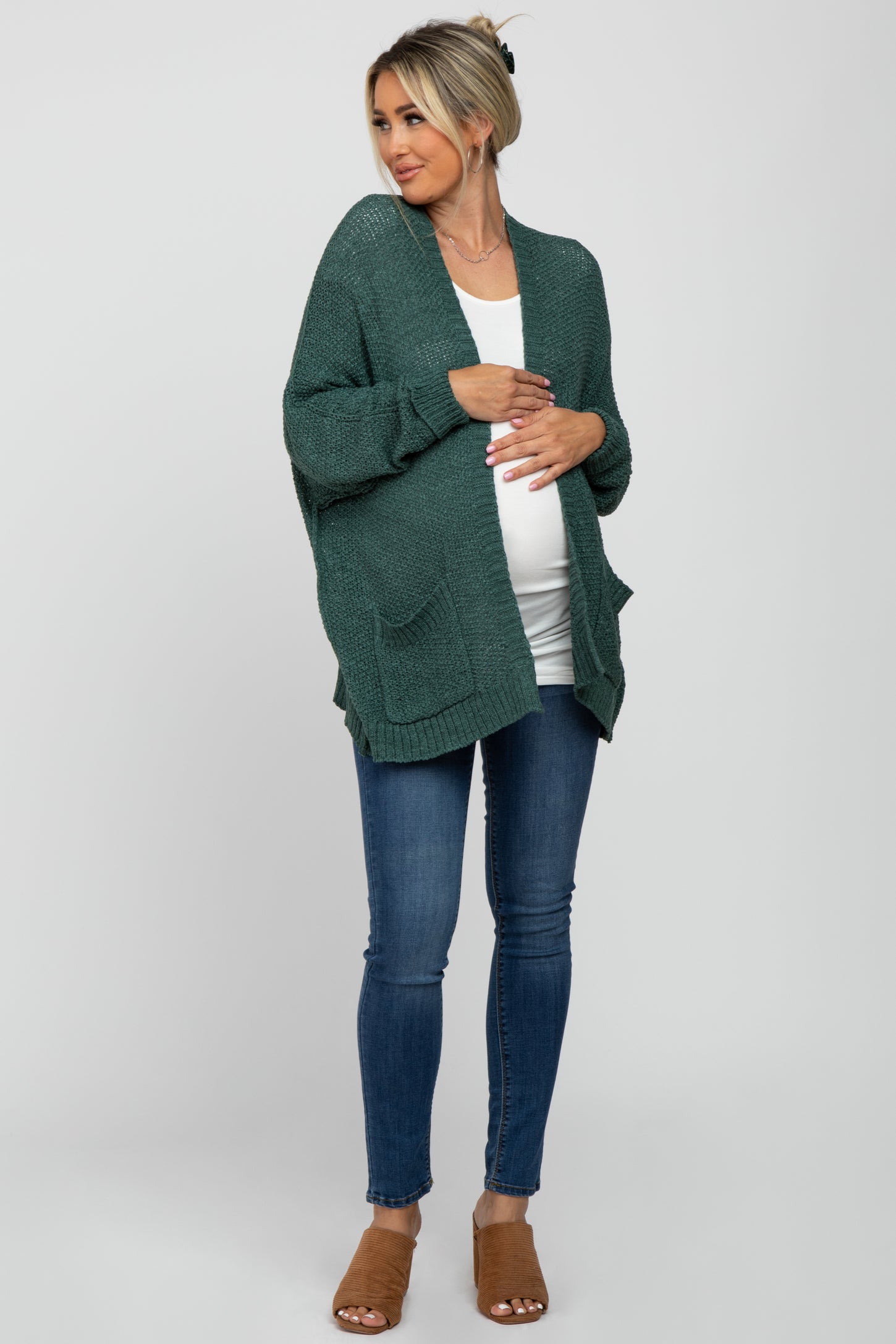 woman wearing a green knit maternity cardigan over a white top, showing her baby bump and paired with blue jeans