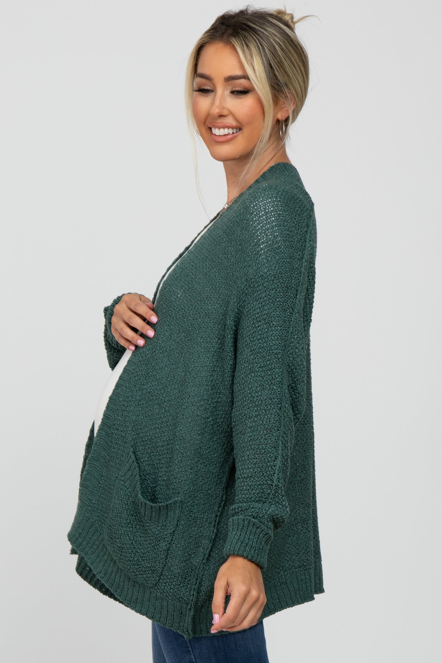 woman wearing a dark green maternity cardigan with pockets and a visible baby bump