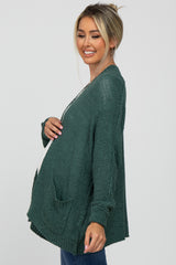 woman wearing a dark green maternity cardigan with pockets and a visible baby bump