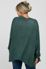 woman wearing a dark green oversized knit maternity sweater styled with casual jeans and a hair clip