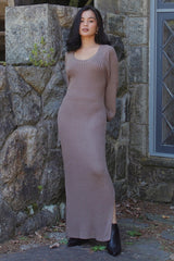 woman wearing a taupe ribbed knit maxi dress with side slits and long sleeves, standing against a stone wall