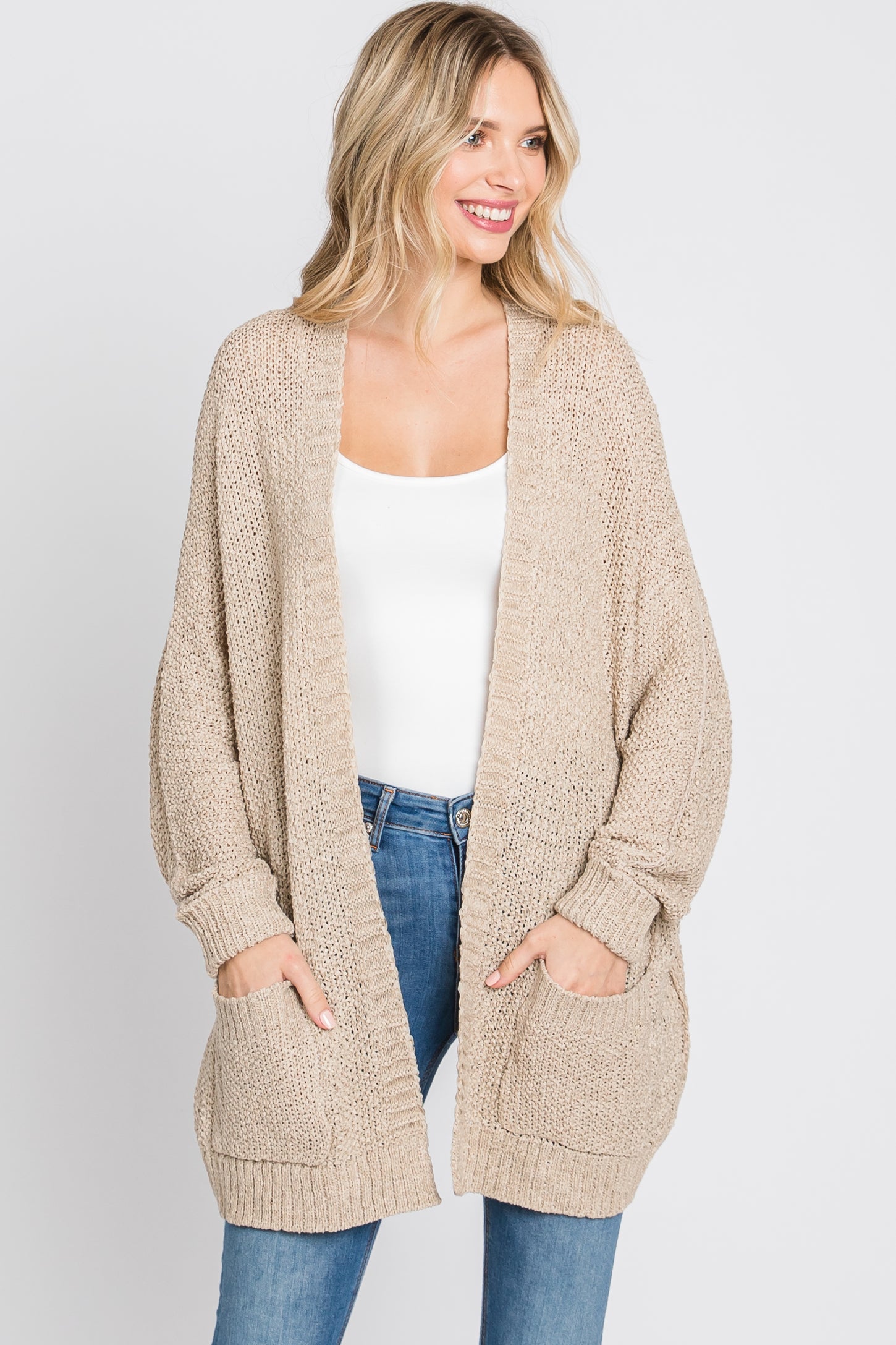 woman wearing a beige oversized knit cardigan with pockets over a white top and blue jeans