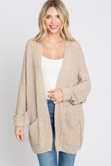 woman wearing a beige oversized knit cardigan with pockets and a white tank top, paired with blue jeans