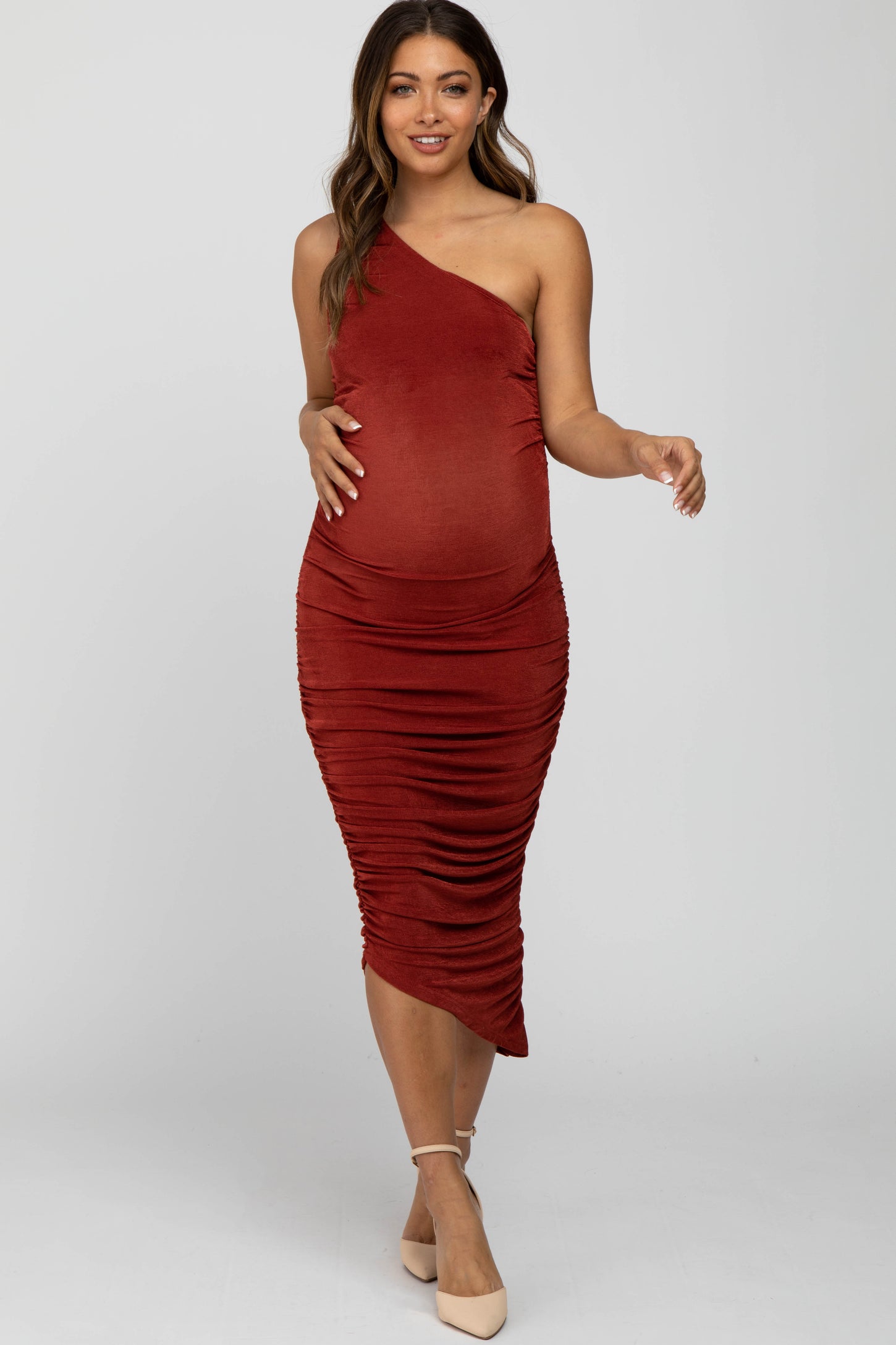 woman wearing a rust one-shoulder maternity dress with ruching and a visible baby bump