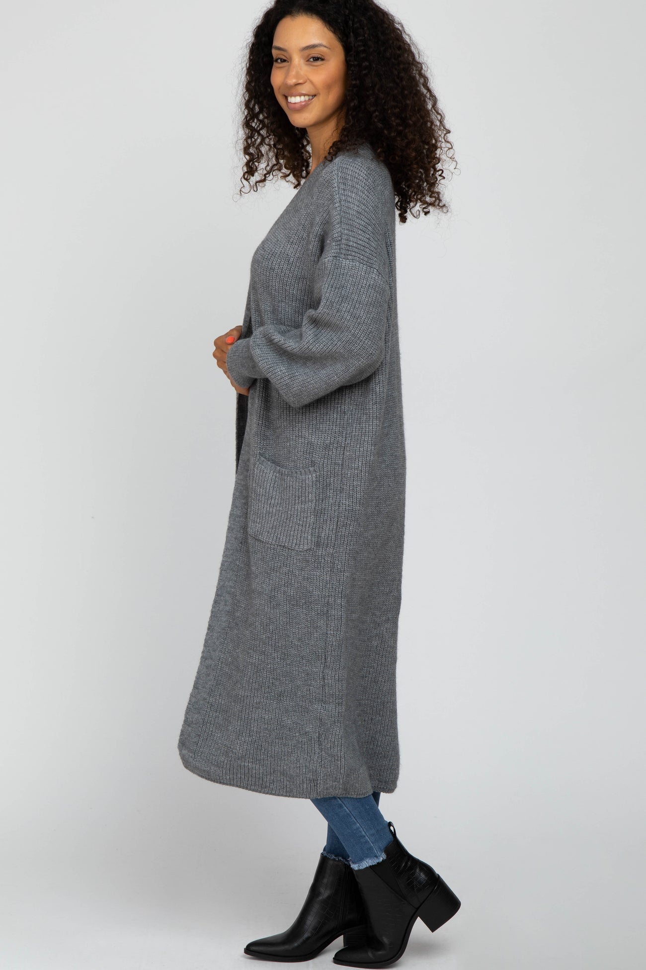 woman wearing a long gray knitted cardigan with pockets, styled with jeans and ankle boots