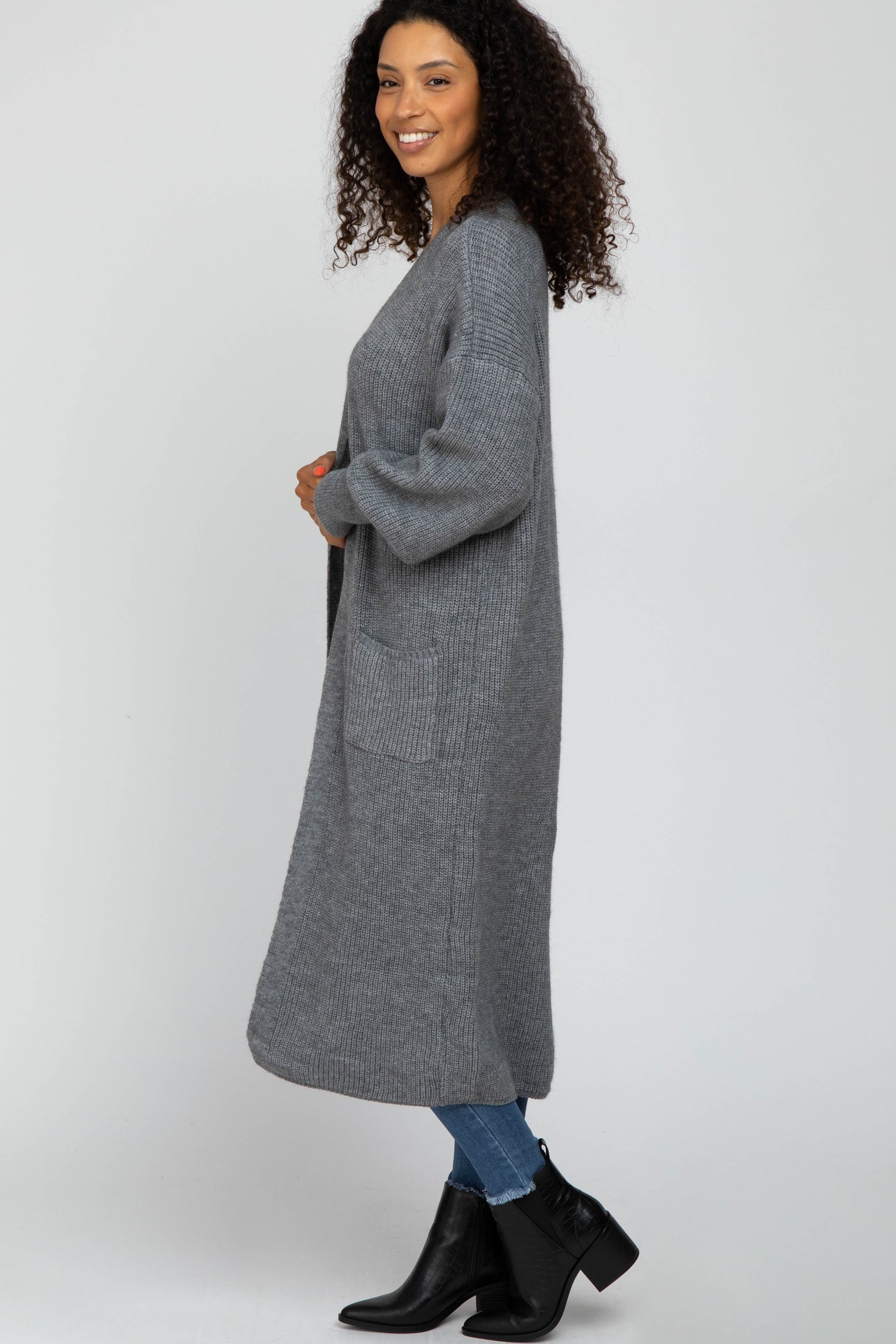 woman wearing a long gray knitted cardigan with pockets, styled with jeans and ankle boots