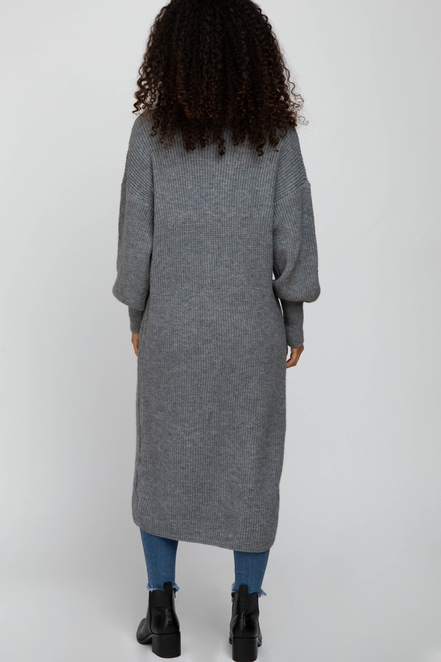 woman wearing a long gray knitted cardigan with oversized sleeves and side slits, viewed from the back