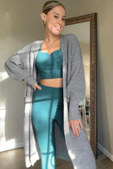 woman wearing a gray long cardigan over a teal crop top and matching high-waisted leggings, posing in front of a mirror