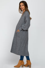 woman wearing a long gray maternity cardigan with pockets and a relaxed fit, paired with blue jeans and tan ankle boots