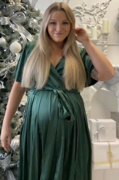 woman wearing a dark green maternity wrap dress with a tie and a visible baby bump, standing in a festive setting