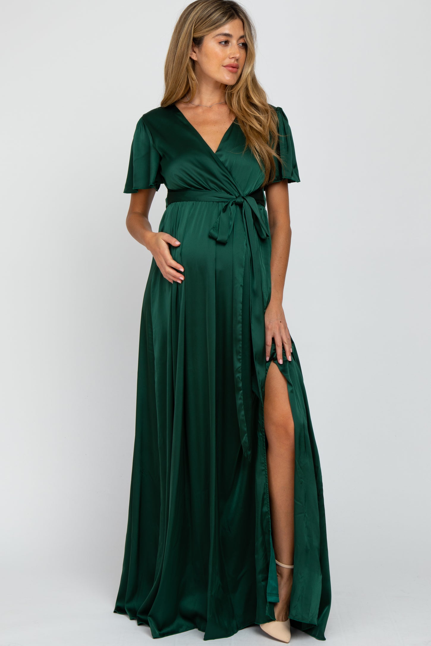 woman wearing a dark green maternity wrap dress with short sleeves and a thigh-high slit, holding her baby bump
