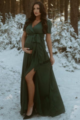 woman wearing a green maternity maxi dress with a wrap design, showing a baby bump in a snowy forest setting