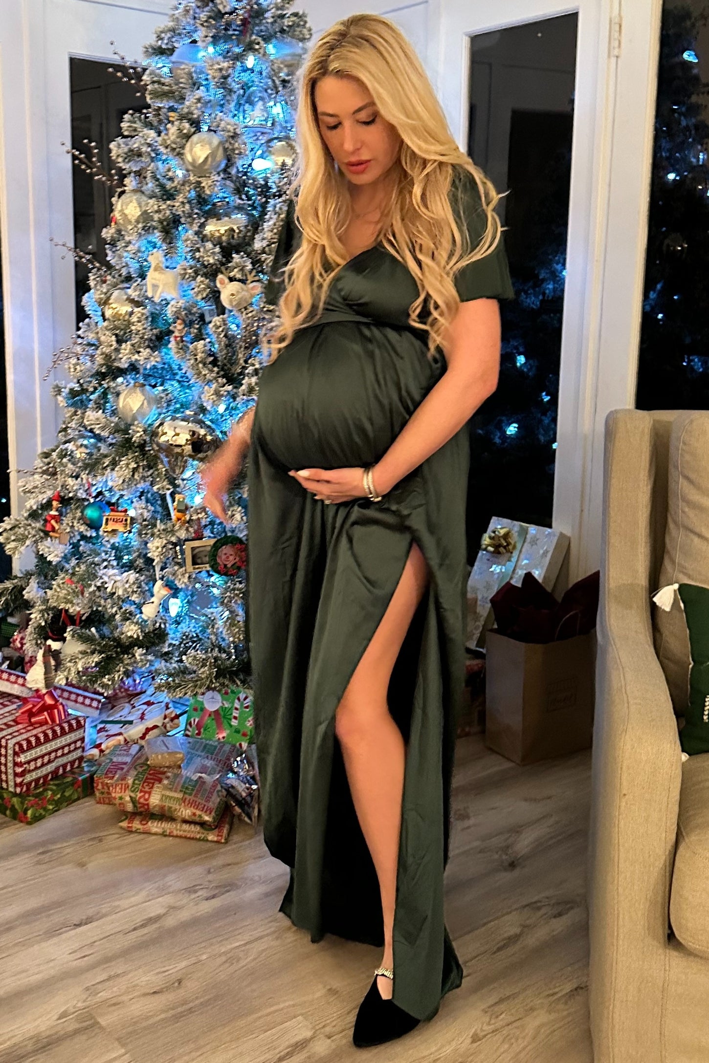 woman wearing a dark green maternity gown with a thigh-high slit, showcasing her baby bump in a festive setting
