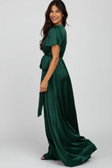 woman wearing a long green satin dress with short puff sleeves and a waist tie, facing sideways