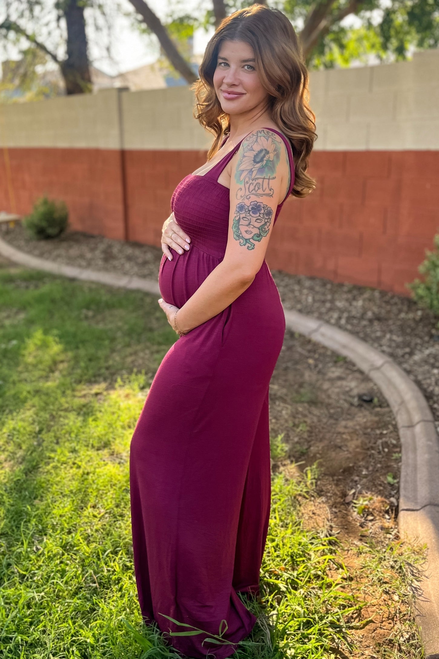 woman wearing a burgundy maternity maxi dress and holding her baby bump in a garden setting